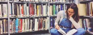 Teaserbild zeigt Person, die in der Bibliothek am Boden sitzt und liest