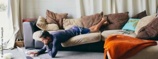 Banner zeigt Person, die am Sofa liegt und am Laptop arbeitet, der am Boden steht