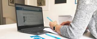 Banner zeigt Person, die an Tisch mit Laptop sitzt und Stift hält