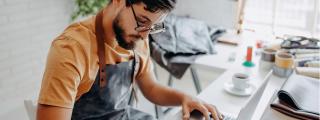 Banner zeigt Person mit Schürze, die am Laptop arbeitet